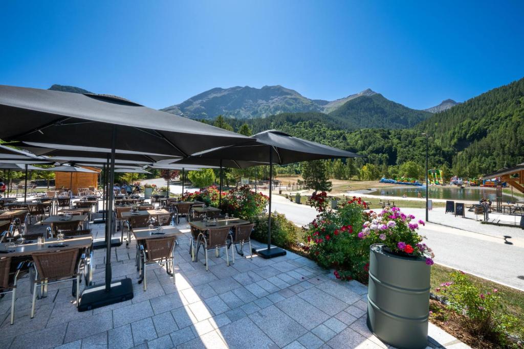 a restaurant with tables and umbrellas with mountains in the background at Hôtel et Camping O2 Orcières Outdoor Area in Orcières