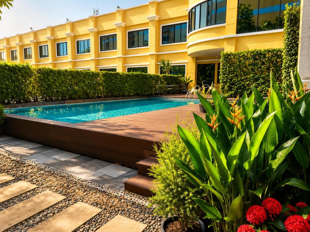 A rectangular outdoor pool beside a landscaped deck and yellow hotel building.