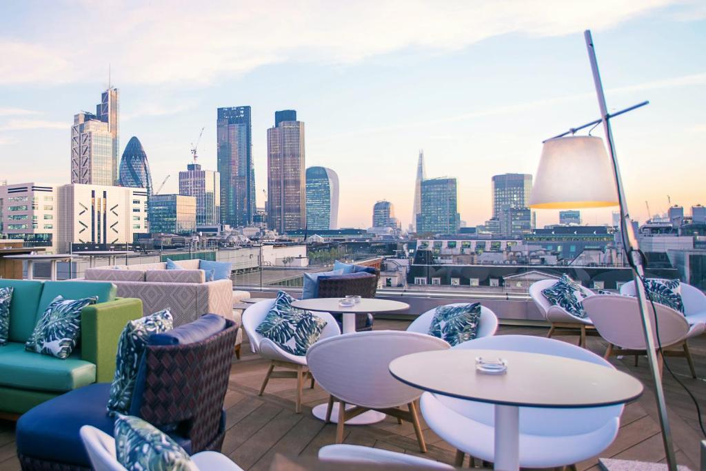 Montcalm Royal London House, London City في لندن: فناء على السطح مع طاولات وكراسي وأفق المدينة