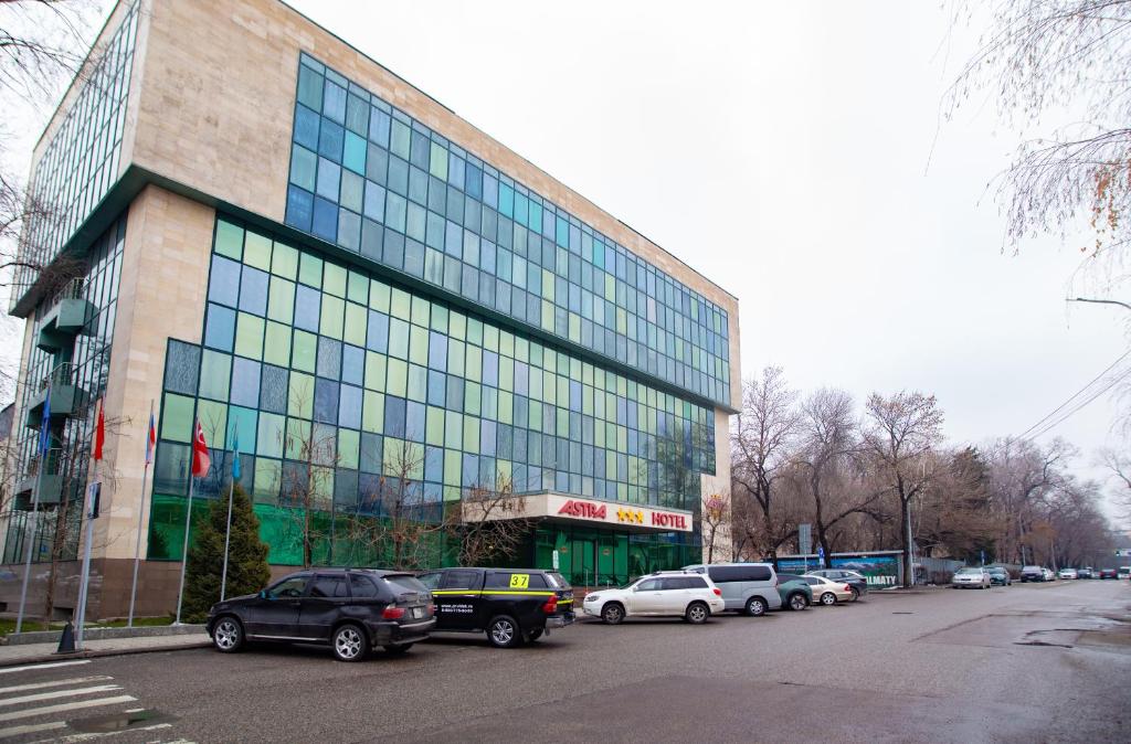 a large glass building with cars parked in front of it at Astra City Hotel in Almaty