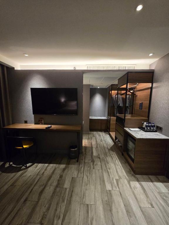 A room work corner with a wall-mounted TV, narrow desk, stool, wardrobe, and beverage station.