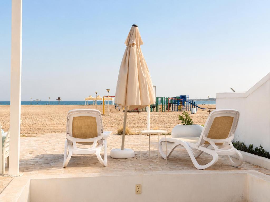 a beach with two chairs and an umbrella and a table at Liora Inside Al Dana beach Resort in Half Moon Bay