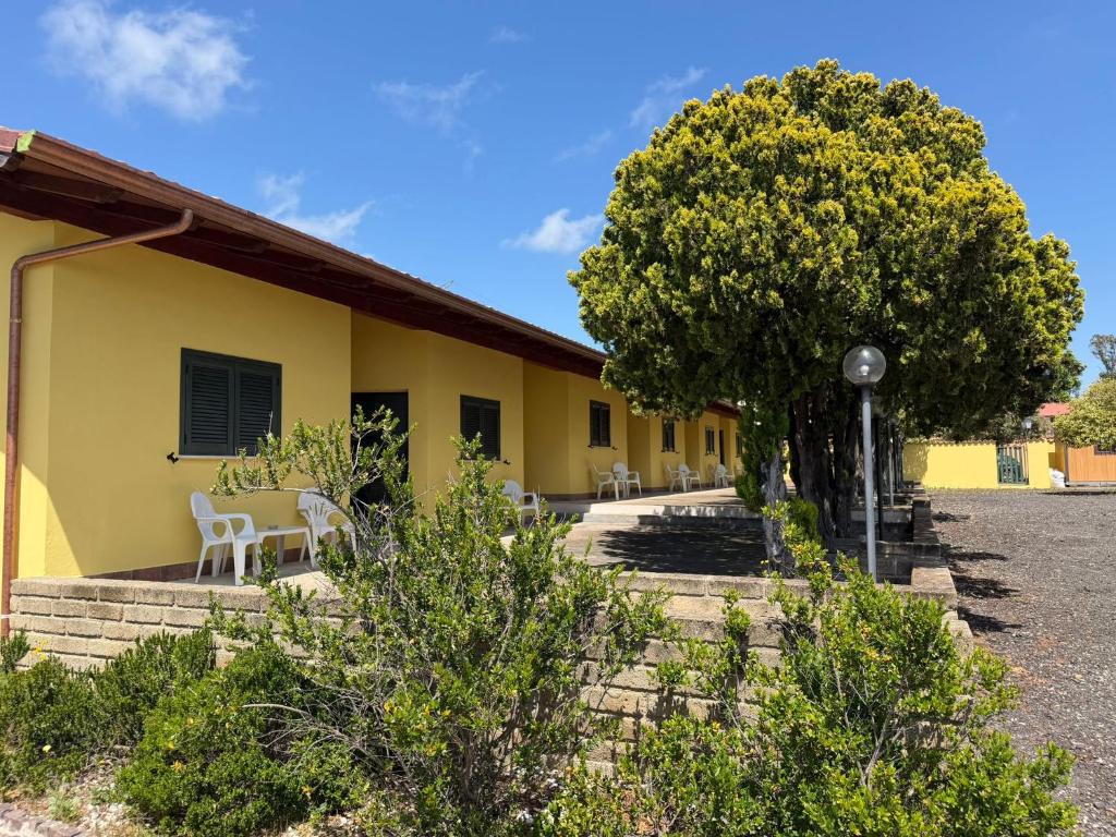 ein gelbes Haus mit Stühlen und einem Baum in der Unterkunft Samarcanda Hotel & Parking di Parmigiani Silvia in Civitavecchia