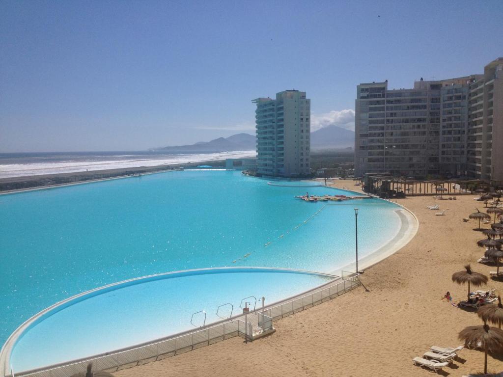a large swimming pool next to a beach with umbrellas at Departamento Resort Laguna del Mar in La Serena