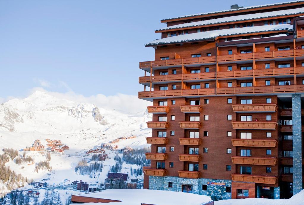 ein hohes Gebäude mit einem verschneiten Berg im Hintergrund in der Unterkunft Residence Les Hauts Bois - maeva Home in Aime La Plagne