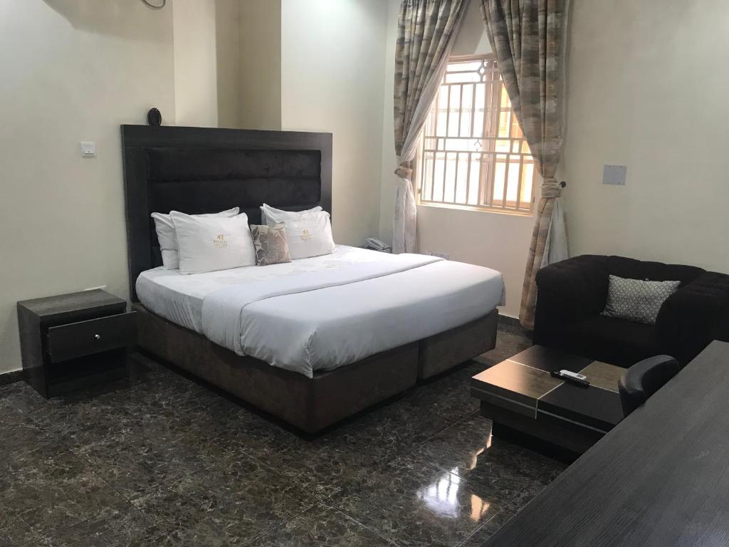 a bedroom with a bed and a chair and a window at ADJ Royalty Hotel & Suites in Benin City