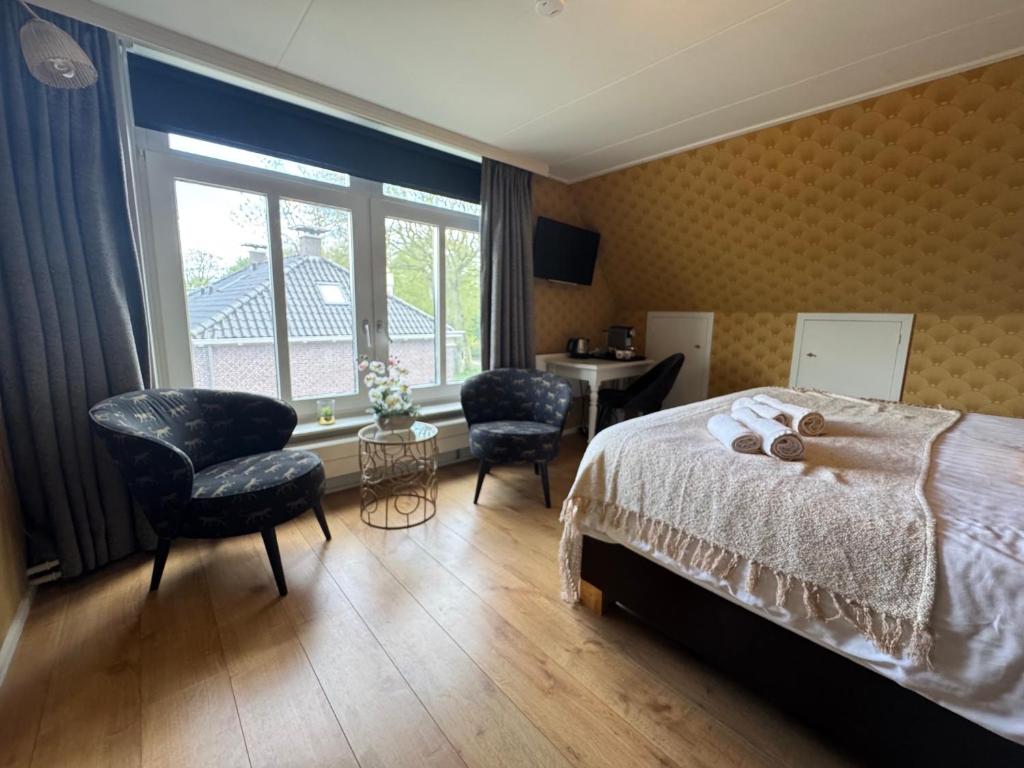 a bedroom with a bed and two chairs and a window at B&B Pastorie Jelsum in Jelsum
