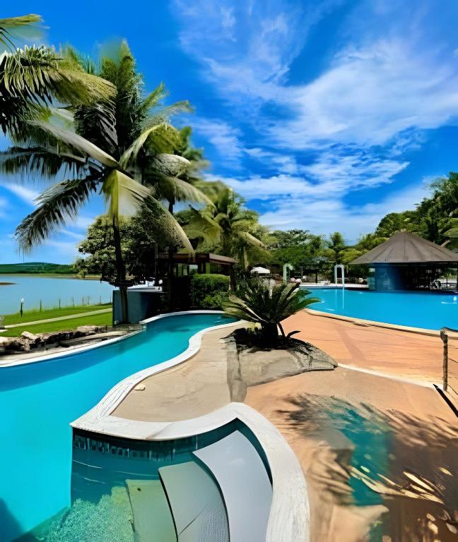 a resort swimming pool with palm trees in the background at Pontal do Lago Flat Residence, aproveite dias incríveis em família às margens do lago Corumbá in Caldas Novas