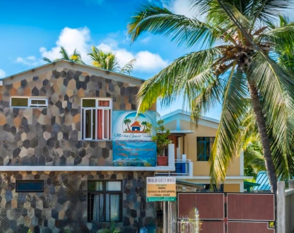 a building with a palm tree in front of it at Merlin Guest House in Rodrigues Island