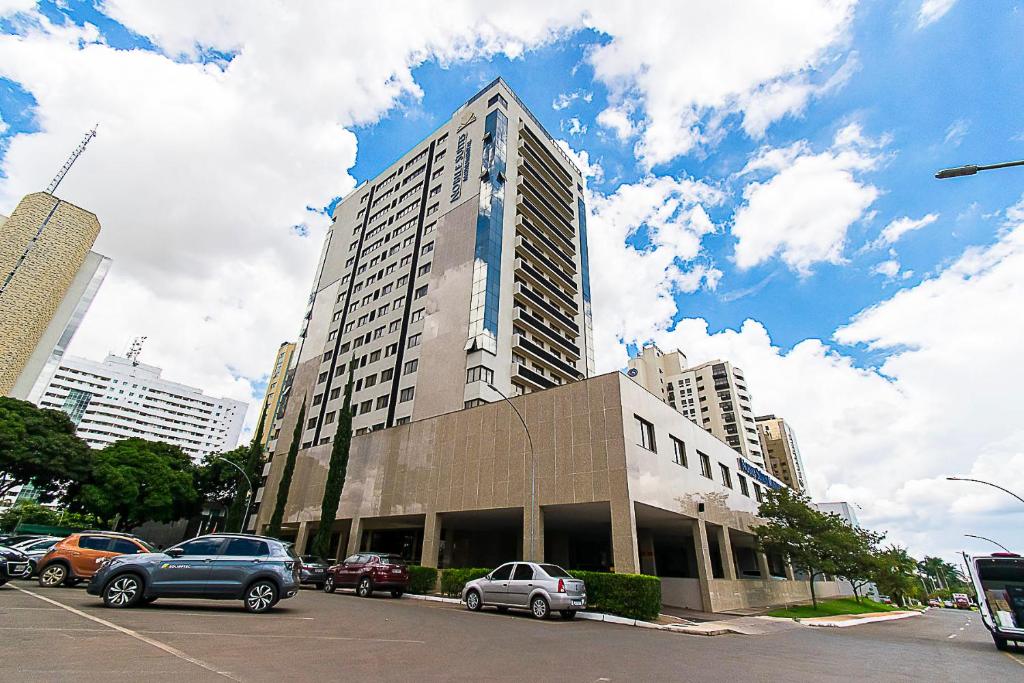 a tall building with cars parked in a parking lot at Nobile Hotel em Brasília 97172 in Brasília