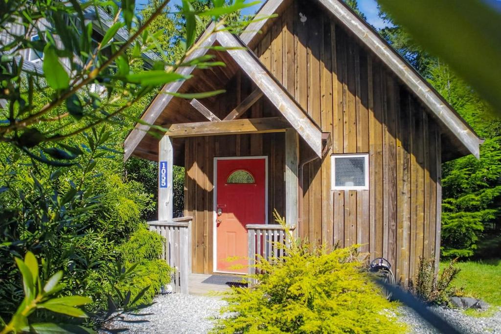a small wooden building with a red door at Rising Tide- Cabin In Ucluelet in Ucluelet