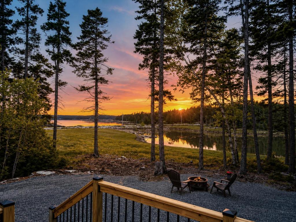 a sunset over a lake with two chairs and a table at Oceanfront Sunset View Cabin in Milbridge