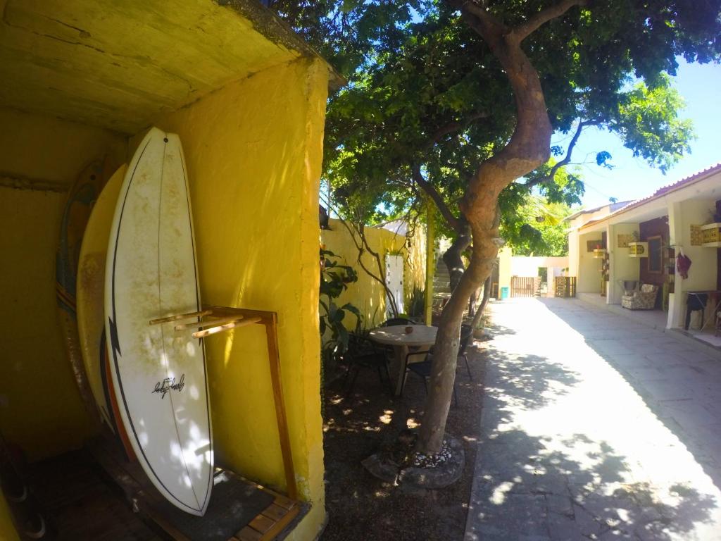 a surfboard leaning against a yellow wall next to a tree at Canto da Onda - Trilha exclusiva para a praia in Marechal Deodoro