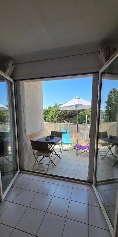 a screened in porch with a table and chairs and an umbrella at Calme et indépendant avec clim, wifi et parking - 2e étage sans ascenseur in Canet-en-Roussillon