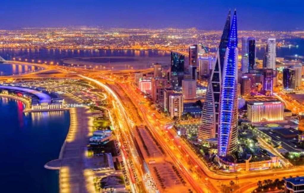 a city lit up at night with a tall building at Fursan Apartment in Manama