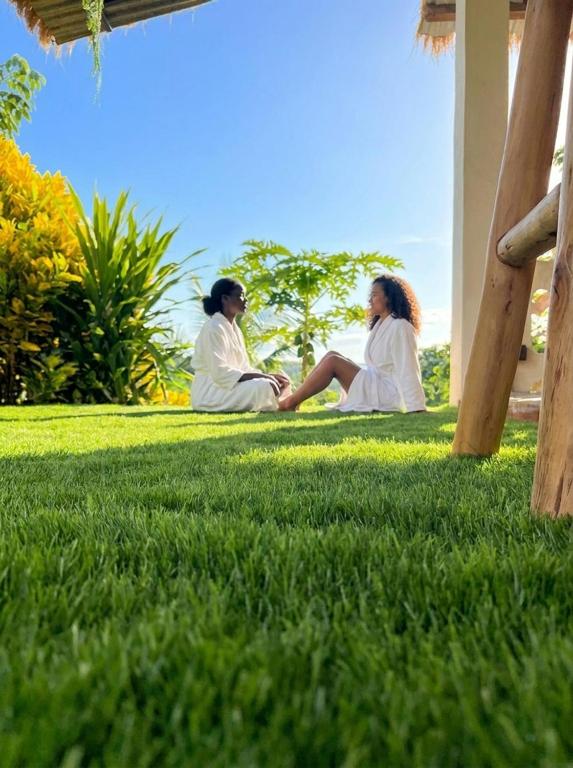 two women in white robes sitting on the grass at LESSENCIEL Villa in Sada