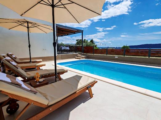 a swimming pool with two chairs and an umbrella at Elegant Holiday House 3D by the Sea with pool and included breakfast in Kaštela