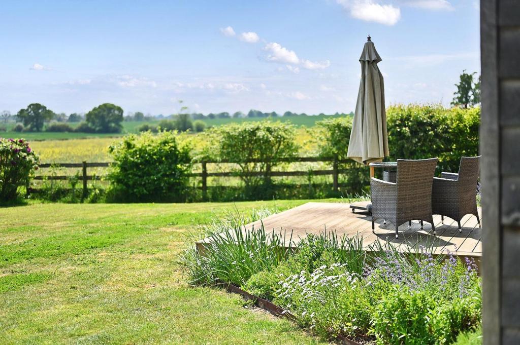 a patio with an umbrella and chairs and a field at Acorn Barn in Ashford