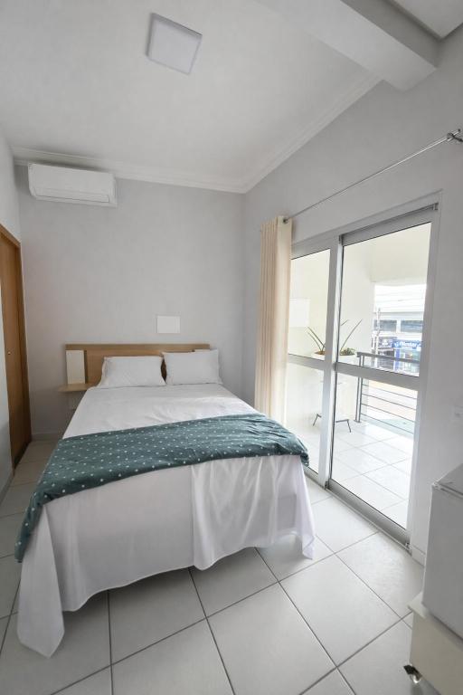a white bedroom with a bed and a large window at DunnaAP Smart Studios in Catalão