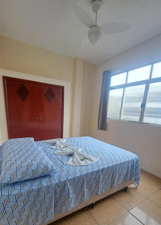 a bedroom with a bed with a blue comforter and a window at Hotel Pousada Angra Encanto in Angra dos Reis