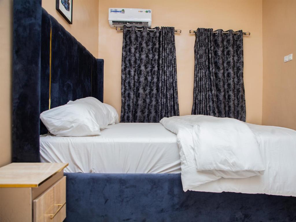 a small bedroom with a bed with a blue headboard and curtains at Radores Apartment in Ayobo