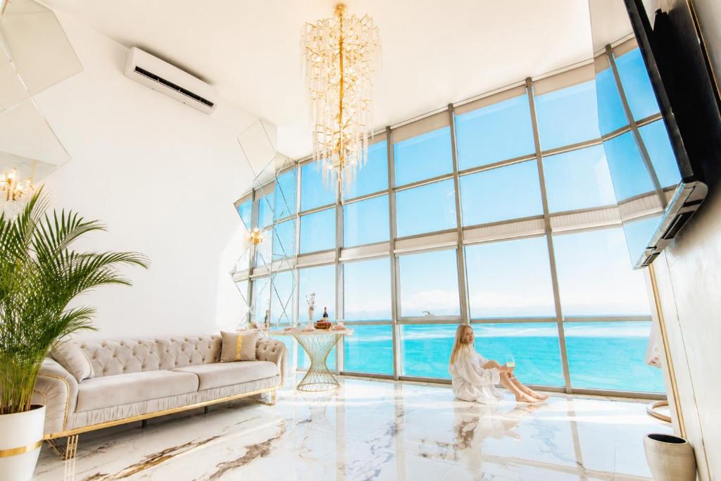 a woman sitting in a living room with a large window at Penthouse Panorama Luxury Sea View Premium Stay in Batumi in Batumi