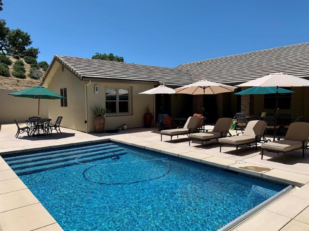 a swimming pool with chairs and umbrellas next to a house at Hilltop Vistas Pool, Wine & Family Fun in Atascadero