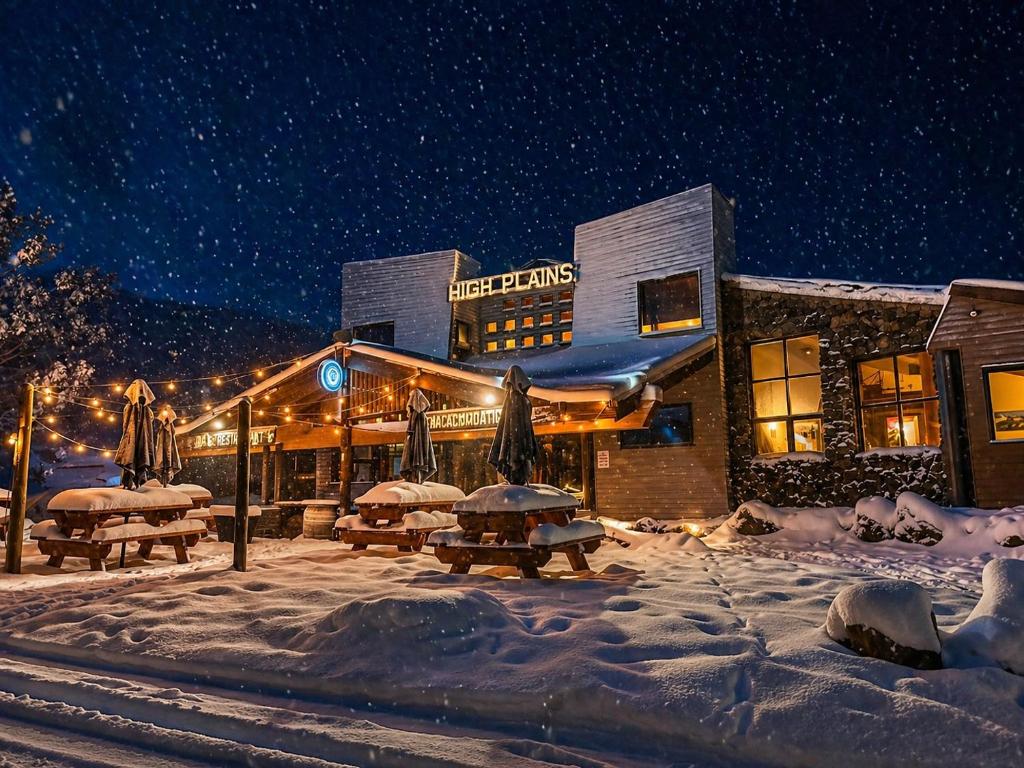 a building with tables and umbrellas in the snow at night at High Plains Lodge Rooms in Dinner Plain