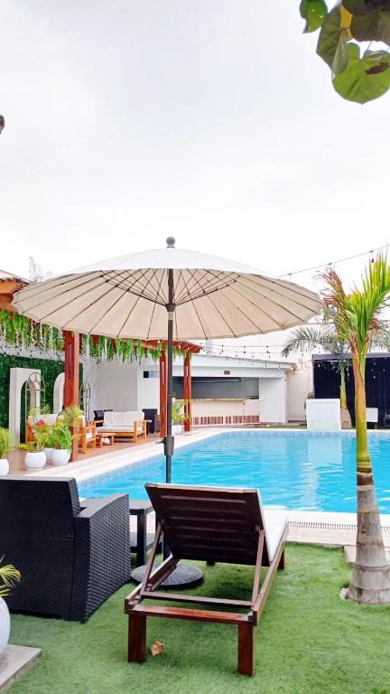 a pool with an umbrella and a chair and a table at Bungalow Jatun Mama in Ventanilla