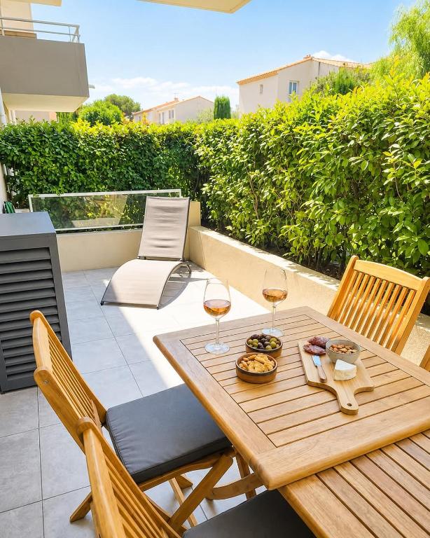 a wooden table with two glasses of wine on a patio at Refuge des Plages-T3 neuf climatisé - Terrasse Sud - proche mer et port à Fréjus in Fréjus