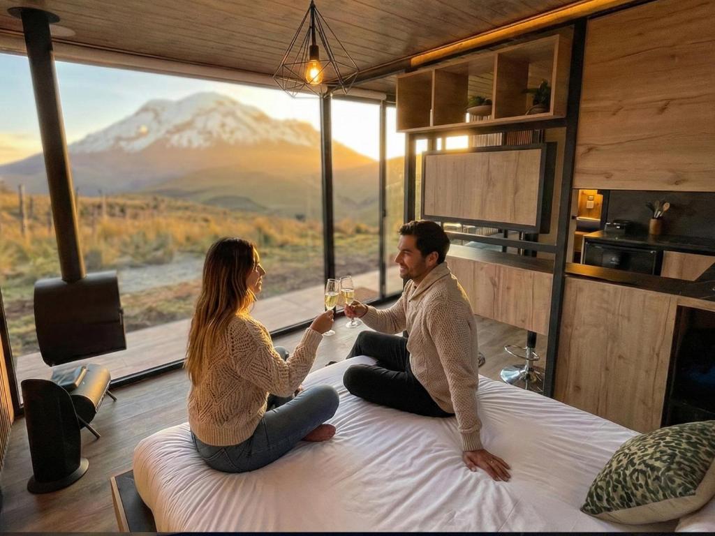 a man and woman sitting on a bed drinking champagne at Tiny house, comfort and peace facing Chimborazo in Riobamba