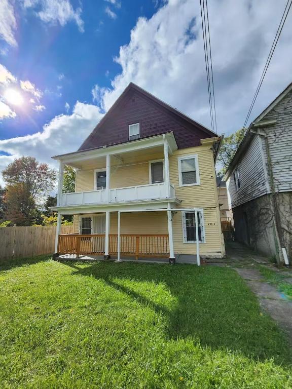 a yellow house with a porch and a fence at Spacious 3BR Niagara Stay + Backyard in Niagara Falls