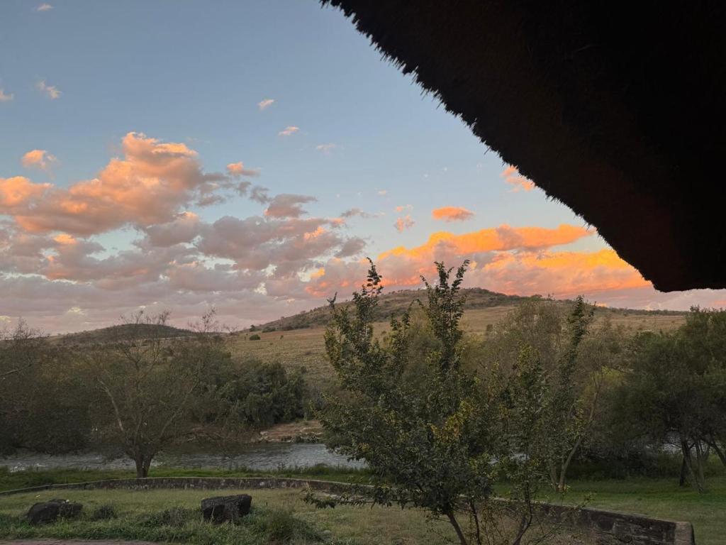 a sunset over a field with a river and trees at Shamwari Guesthouse in Kalkheuvel
