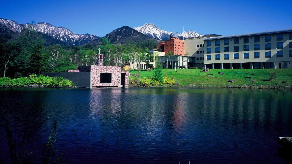 a building next to a lake with mountains in the background at Kiyosato Kogen Resort in Hokuto