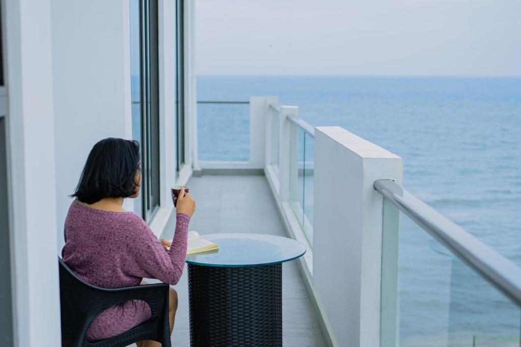 a woman sitting at a table looking at the ocean at Marine Suites in Colombo