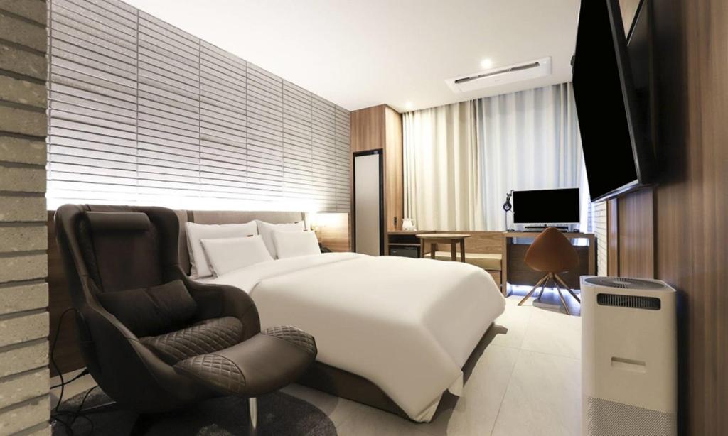 a bedroom with a white bed and a chair at Wonju Brown Dot Hotel Corporate city in Wonju