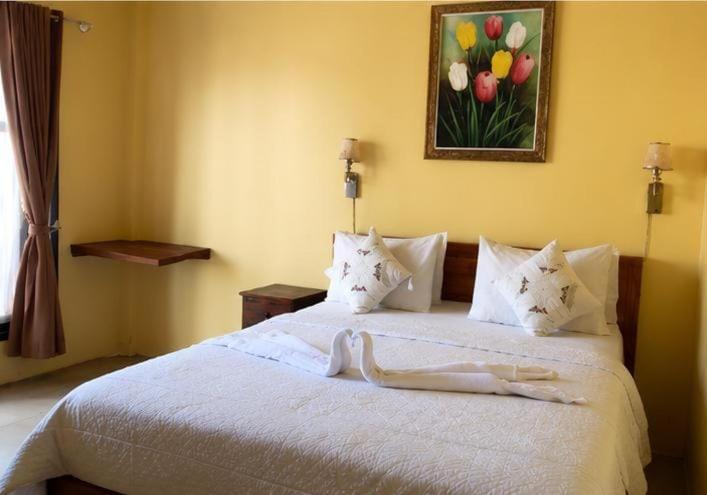 a bedroom with a white bed with a painting on the wall at Deva Devi Beach Inn in Sampalan