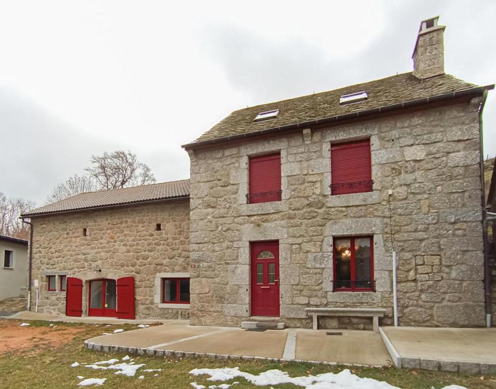 a stone building with red doors and a bench in front at Digitales en margeride in SAINT DENIS EN MARGERIDE