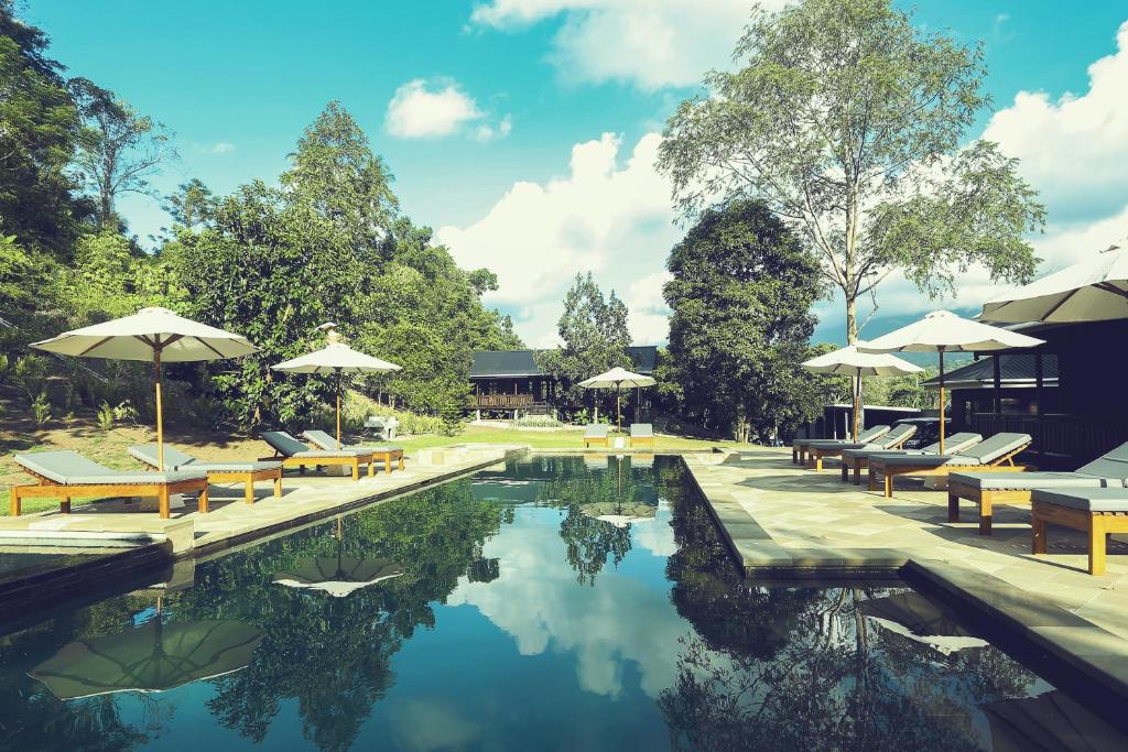 a swimming pool with tables and umbrellas and chairs at Bobocha Tangkoko Nature Resort in Bitung