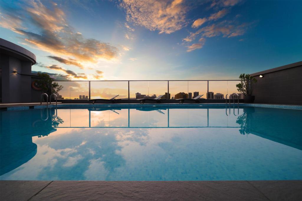 A rooftop pool reflects a vivid sunset over the Kuala Lumpur skyline.
