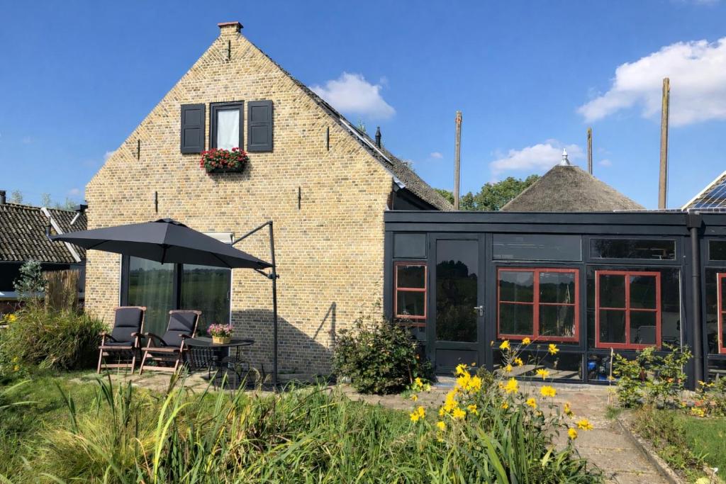 a brick house with two chairs and an umbrella at B&B De Beijersche Stee, Logies aan de Waterkant in Stolwijk