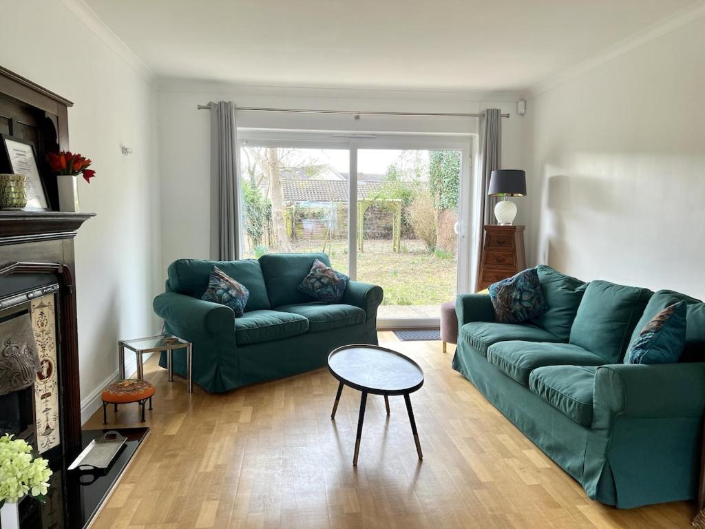 a living room with two green couches and a table at Large Stylish 5 bed Cambridge House in Harston