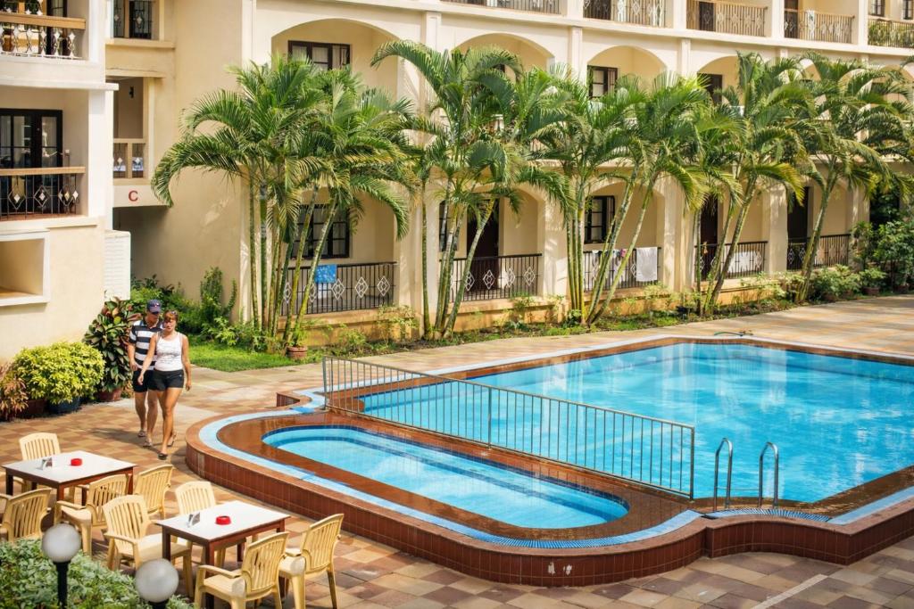a woman walks by a swimming pool in a hotel at Riverside Regency Resort in Baga