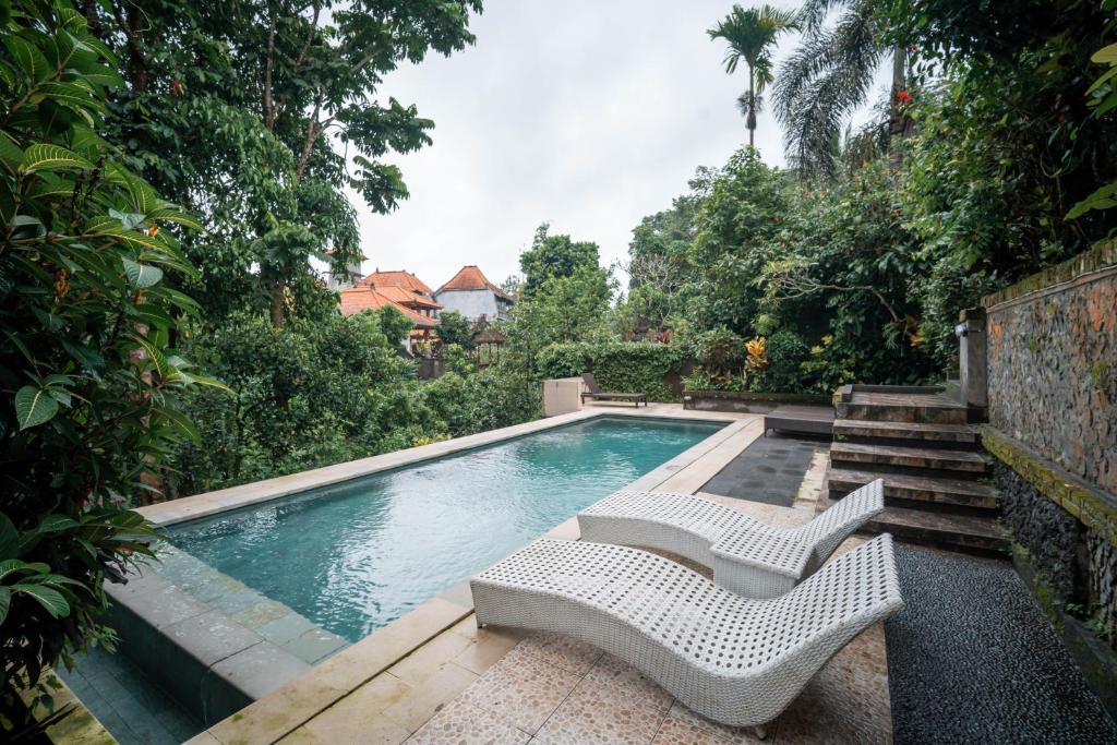 a swimming pool with two white chairs sitting next to it at Bismajaya Bungalow in Ubud