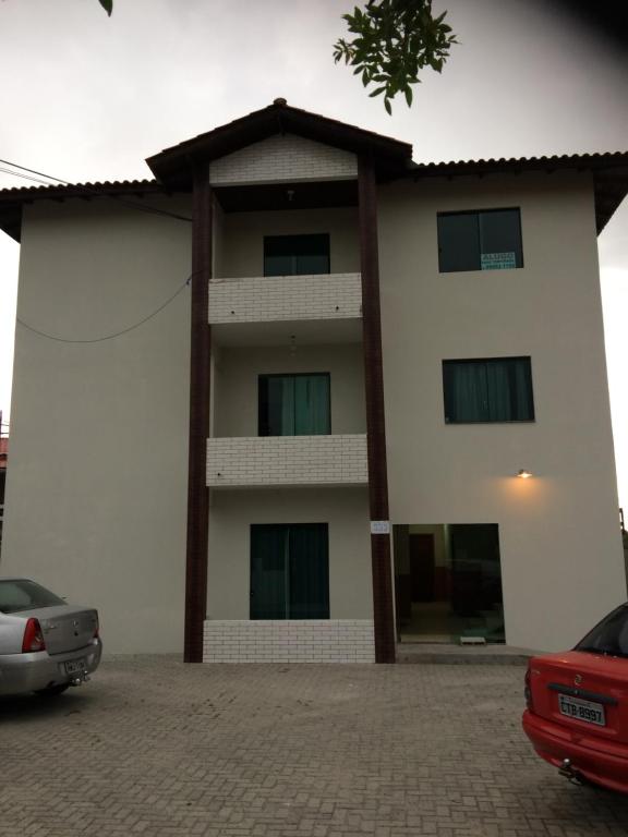 un gran edificio blanco con un coche rojo aparcado delante en Abner Residencial, en Florianópolis