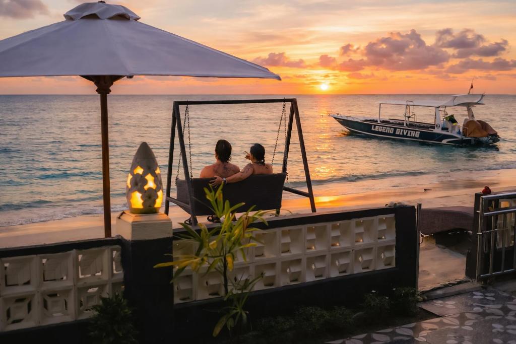 two people sitting in a swing on the beach with a boat at Road Beach Cottages in Nusa Penida