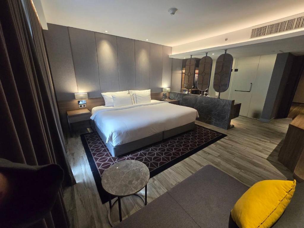 A polished hotel bedroom with a large bed, lounge seating and a partially visible bathroom area.