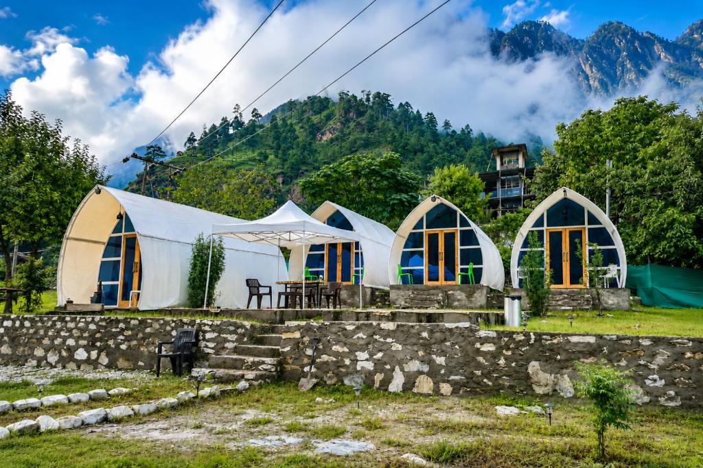 a group of tents in a field with mountains in the background at Vintage Vista Camps in Kasol