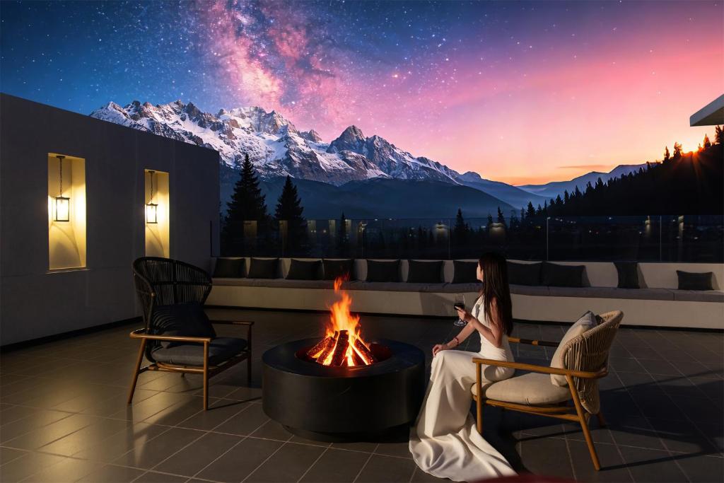 a woman sitting next to a fire pit with a view of the mountains at Lijiang Chenxi View Hotel in Lijiang