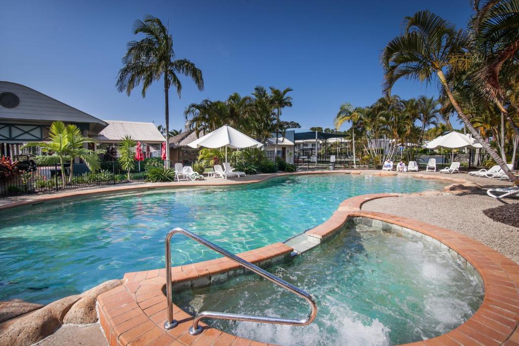 a large swimming pool with blue water and palm trees at Ivory Palms Resort Noosa in Noosaville